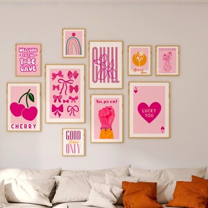 May include: A wall gallery featuring nine framed prints with pink and white designs. The prints include text such as "Welcome to the Babe Cave", "Cherry", "Good Vibes Only", "Yes, you can!" and "Lucky You".