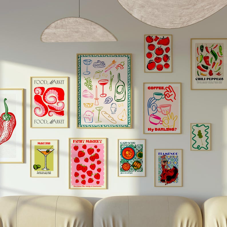 May include: A wall gallery featuring colorful illustrations of food and drinks. The illustrations include a martini, chili peppers, strawberries, a food market, coffee, gazpacho, and flamenco dancers. The illustrations are framed in a light wood frame and are hung on a white wall.