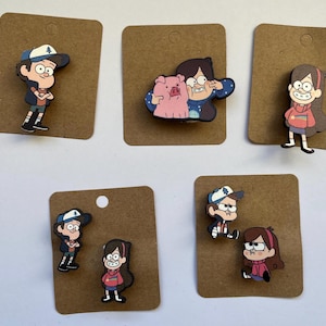 Puede incluir: Conjunto de 6 pines de personajes de Gravity Falls en cartulina marrón. Los pines presentan personajes del programa, incluidos Dipper, Mabel, Stan y Waddles.