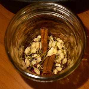 Könnte beinhalten: Ein Glasgefäß gefüllt mit getrockneten Jasminblüten und Zimtstangen. Das Gefäß steht auf einer Holzoberfläche.