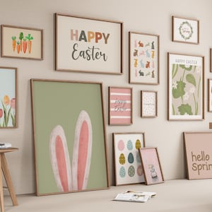 May include: A gallery wall featuring various framed prints with Easter and spring themes, including illustrations of carrots, tulips, colorful eggs, rabbits, and text reading Happy Easter, March 28, and hello Spring, displayed on a light beige wall.