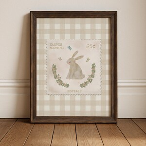Pu&ograve; includere: Opera d'arte incorniciata con un design di francobollo a tema pasquale. Il francobollo raffigura un coniglietto seduto, farfalle ed elementi floreali, con il testo "EASTER MORNING" e "POSTAGE". Lo sfondo &egrave; un motivo a scacchi beige e bianco.