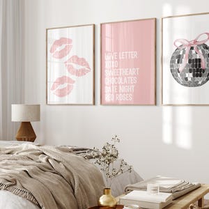 May include: Three framed prints with pink backgrounds. The left print features three pink lips, the middle print has the text "Love Letter XOXO Sweetheart Chocolates Date Night Red Roses", and the right print shows a silver disco ball with a pink ribbon.