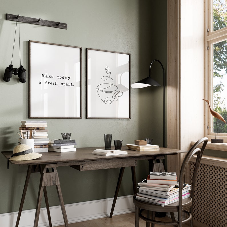May include: A home office setup featuring a wooden desk, chair, and a floor lamp. Two framed prints adorn the wall, one with the text "Make today a fresh start." and the other a line drawing of a coffee cup. Binoculars hang on the wall.