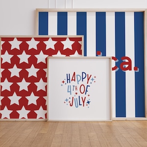 May include: Three framed art prints with patriotic themes. One features a red background with white stars, another has blue and white stripes, and the third says "Happy 4th of July" in red and blue. The frames are light wood.