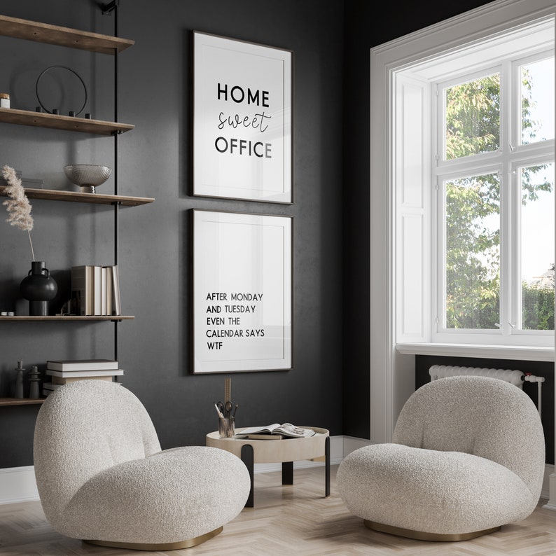 May include: Interior shot of a home office with two framed prints on a dark grey wall. One print reads "HOME sweet OFFICE," and the other says "AFTER MONDAY AND TUESDAY EVEN THE CALENDAR SAYS WTF." Two cream-coloured, rounded armchairs sit on a wood floor.