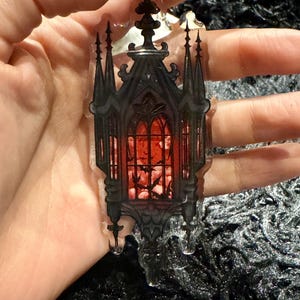May include: A black and red gothic-style window with bats flying inside. The window is made of clear acrylic and has a 3D effect.