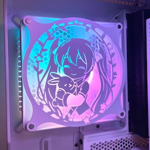 May include: A white computer fan with a cut-out design featuring an anime-style character holding a bunny. The fan has a square frame with rounded corners and is illuminated with blue, pink, and purple lighting.