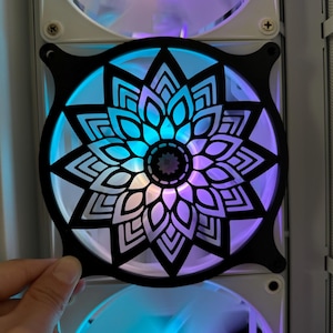 May include: A black computer fan cover with a white and purple mandala design. The fan cover is illuminated with blue and purple light.