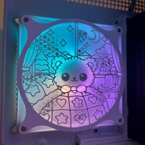 May include: A white computer fan with a cutout design of a cartoon bear sleeping in a bed with stars and hearts. The fan is lit with a blue and purple gradient.