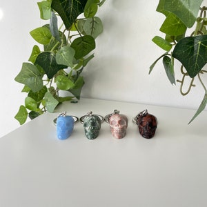 Puede incluir: Cuatro llaveros con forma de calavera hechos de diferentes tipos de piedra. Los llaveros est&aacute;n dispuestos en una fila de izquierda a derecha: azul claro, verde, rosa y rojo oscuro.