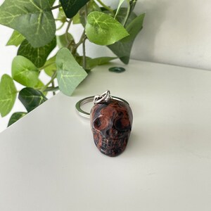 Puede incluir: Un llavero de calavera de m&aacute;rmol rojo y negro. La calavera est&aacute; unida a un anillo de metal plateado.