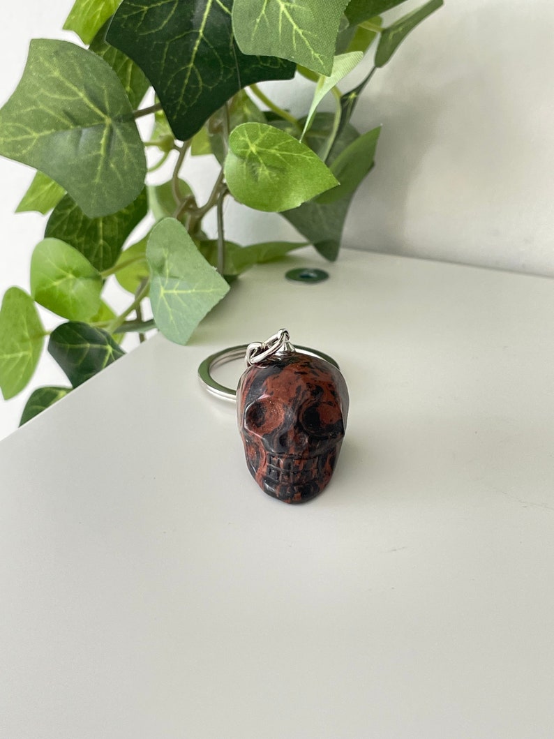 Puede incluir: Un llavero de calavera de m&aacute;rmol rojo y negro. La calavera est&aacute; unida a un anillo de metal plateado.