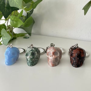Puede incluir: Cuatro llaveros con forma de calavera hechos de diferentes tipos de piedra. Las calaveras son de color azul, verde, marr&oacute;n y rojo.