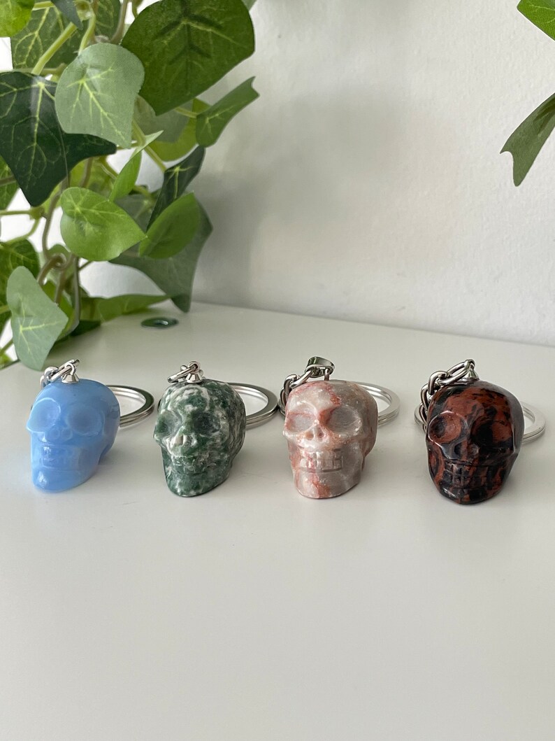 Puede incluir: Cuatro llaveros con forma de calavera hechos de diferentes tipos de piedra. Las calaveras son de color azul, verde, marr&oacute;n y rojo.