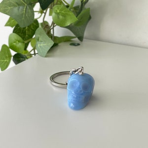 Puede incluir: Un llavero de calavera azul claro con un anillo de metal plateado.