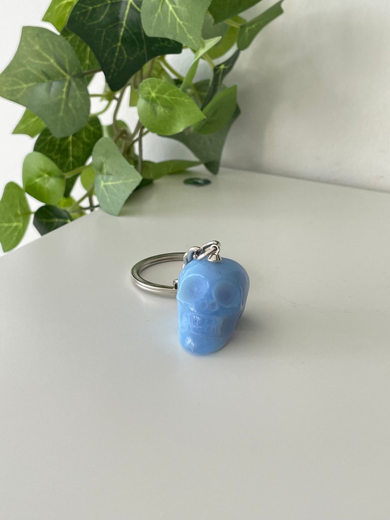 Puede incluir: Un llavero de calavera azul claro con un anillo de metal plateado.