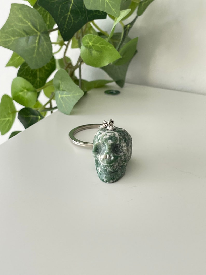 Puede incluir: Llavero de calavera de piedra verde y blanca. La calavera est&aacute; tallada en una piedra verde y blanca con un anillo plateado.