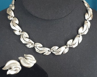 May include: A silver necklace and earrings set with a leaf design. The necklace is made of linked leaves and the earrings are a single leaf shape.