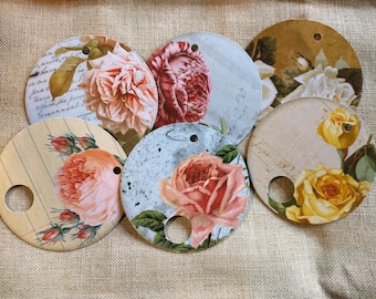 May include: Six round paper tags with floral designs. Each tag has a hole punched in the top and features a different floral pattern with roses, leaves, and handwritten text.