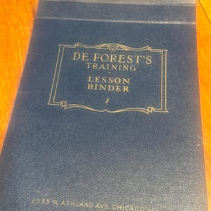 May include: A blue, leather-bound binder with gold lettering that reads "De Forest's Training Lesson Binder" and "2533 N Ashland Ave. Chicago, Ill."