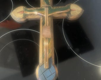 May include: A wooden cross with a painted design in shades of green, yellow, blue, and red. The cross has a gold-colored metal figure of Jesus Christ attached to it.