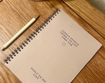 May include: A beige spiral bound notebook with the text "THINGS PEOPLE THINK I'VE GOT TIME FOR" and a small heart symbol. The notebook also has the text "DAILY TO DO LIST" at the bottom.