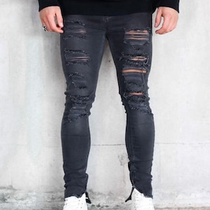 May include: Black distressed skinny jeans with zipper detailing at the ankles. The jeans have several rips and tears throughout the legs.