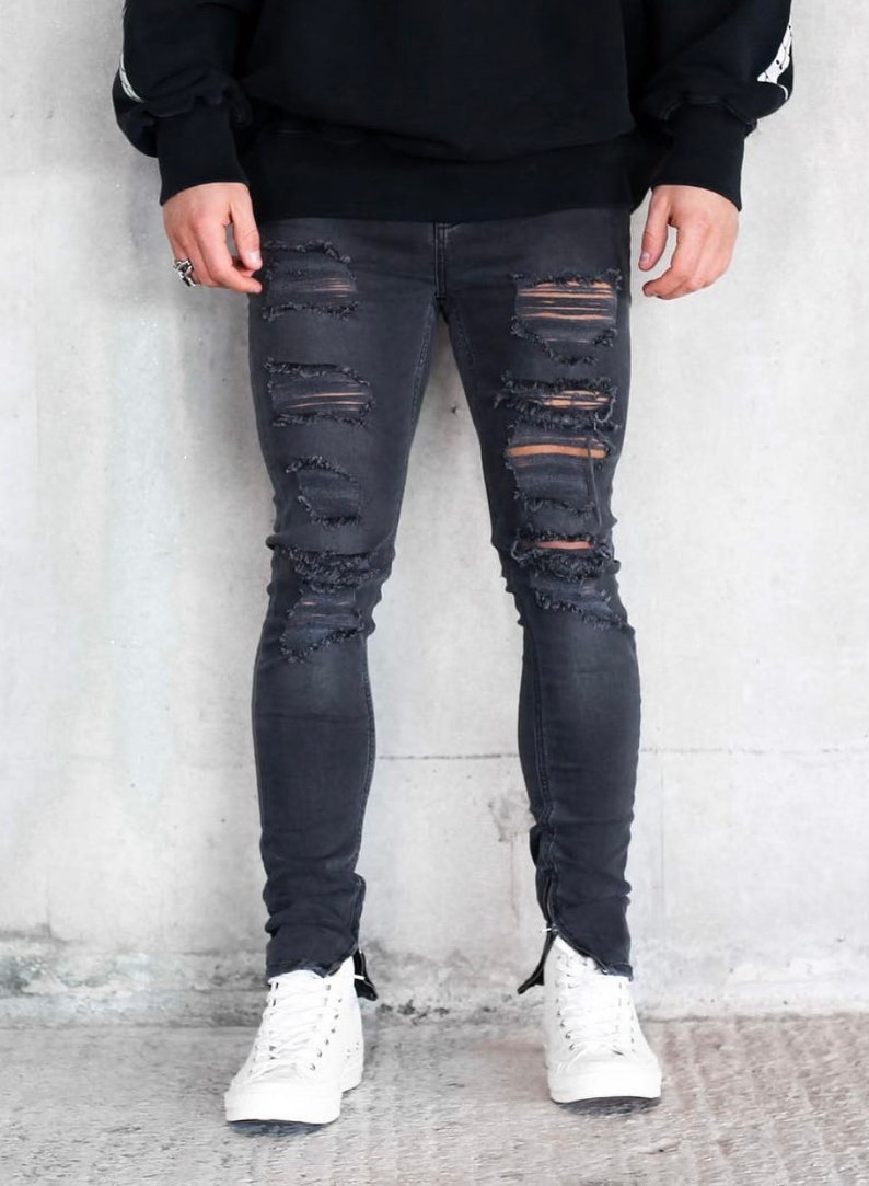 May include: Black distressed skinny jeans with zipper detailing at the ankles. The jeans have several rips and tears throughout the legs.