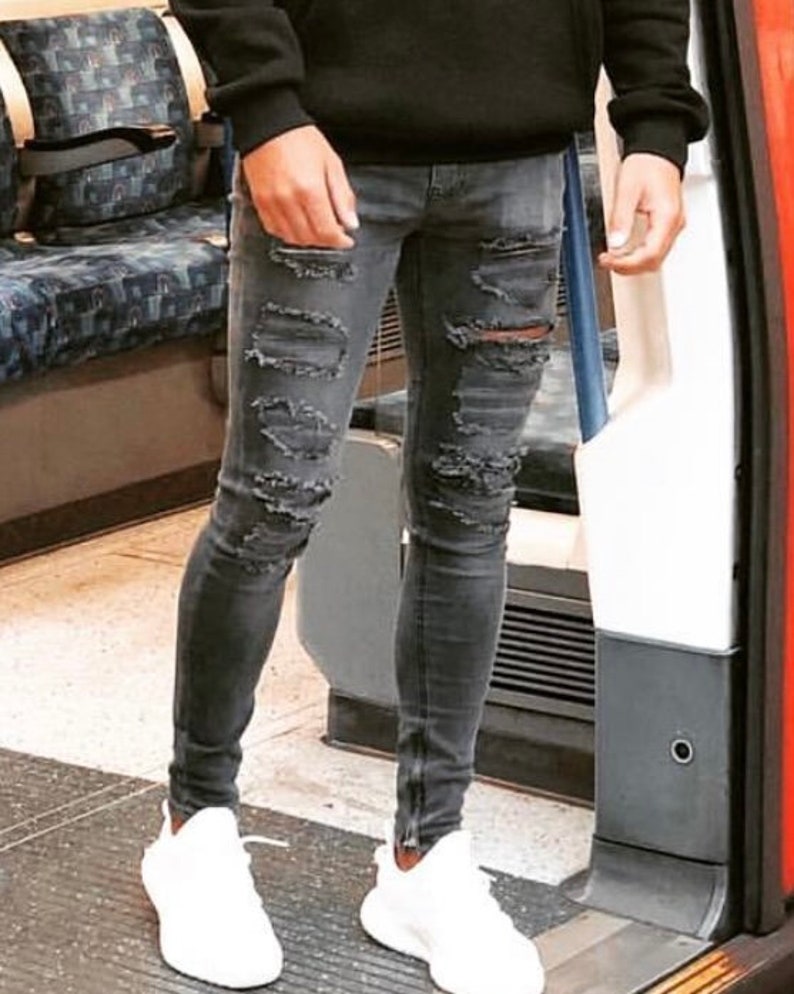 May include: A person wearing gray distressed skinny jeans with zipper details and white sneakers.
