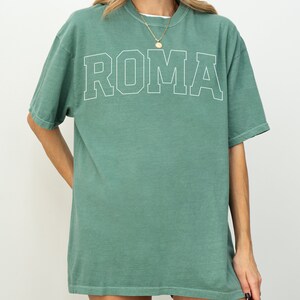 May include: A green oversized t-shirt with the word "ROMA" printed in white on the front.