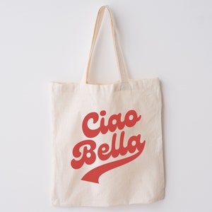 May include: A white canvas tote bag with red text that says "Ciao Bella" in a retro font. The text is in a red, curved, baseball-style font.