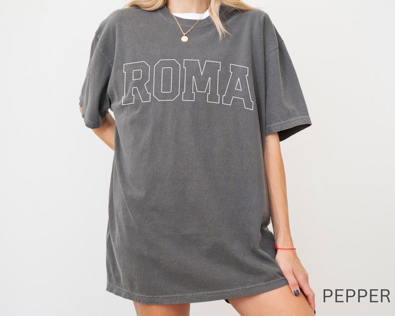 May include: A charcoal gray oversized t-shirt with a white outline of the word "ROMA" printed on the front.