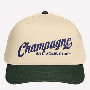 May include: A cream-colored baseball cap with a dark green brim and a dark green button on top. The cap features the word "Champagne" in a navy blue script, with "S'il vous plaît" below it.