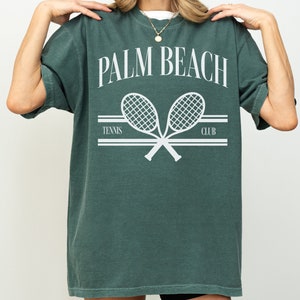 May include: A green t-shirt with the text "PALM BEACH TENNIS CLUB" and a graphic of two crossed tennis rackets.