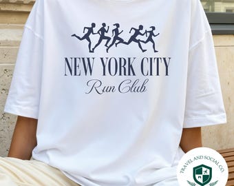 May include: White oversized t-shirt with a navy blue graphic of running figures above the text "NEW YORK CITY Run Club." The shirt also features a small logo for "TRAVEL AND SOCIAL CO." at the bottom right.