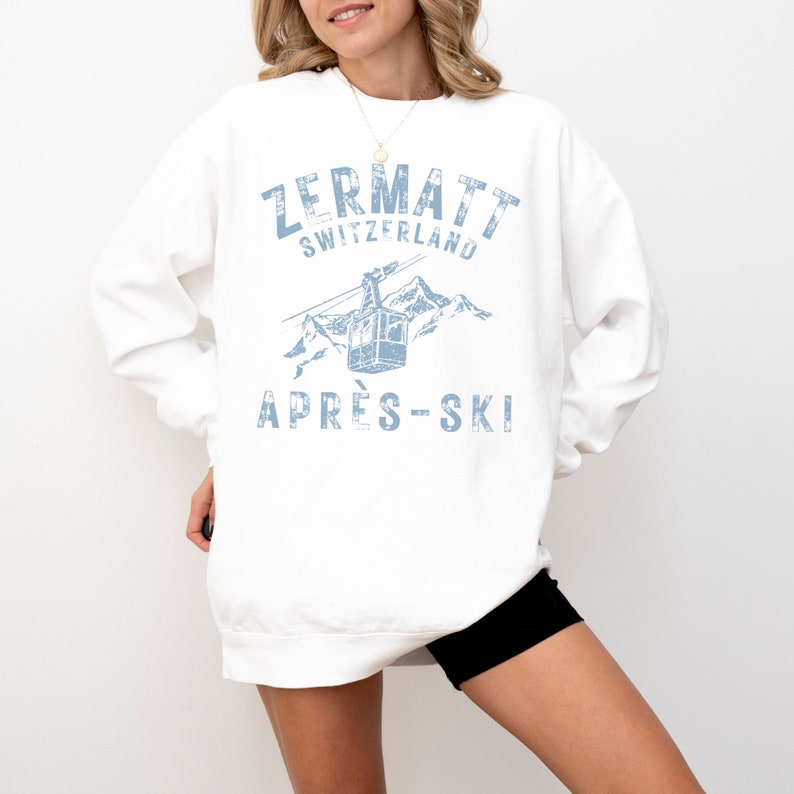 May include: White sweatshirt with a blue graphic print of a ski lift in the mountains. The text "Zermatt Switzerland" and "Apr&egrave;s-Ski" is printed on the sweatshirt.