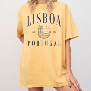 Puede incluir: Camiseta amarilla con un gr&aacute;fico azul marino de un castillo y el texto "LISBOA EST 1147 PORTUGAL"