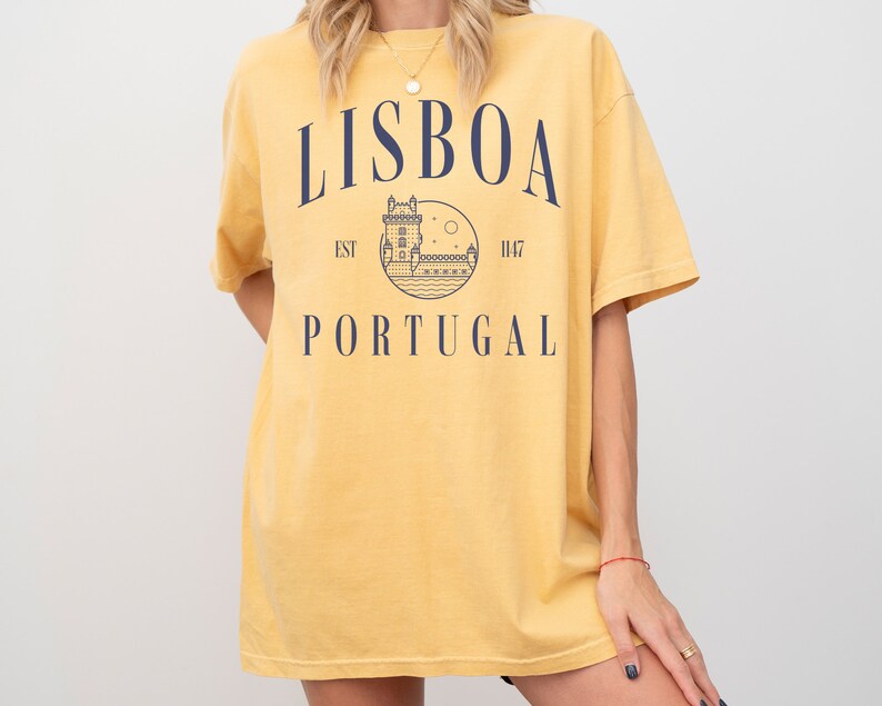Puede incluir: Camiseta amarilla con un gr&aacute;fico azul marino de un castillo y el texto "LISBOA EST 1147 PORTUGAL"