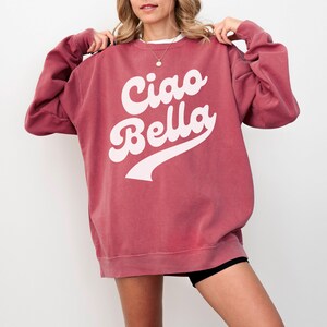 Puede incluir: Una sudadera color granate con un gr&aacute;fico blanco que dice "Ciao Bella" en una fuente retro.