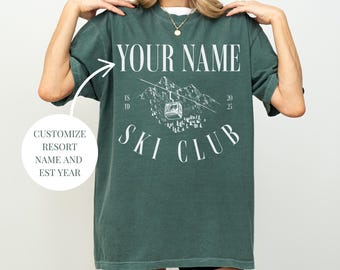 Könnte beinhalten: Ein grünes T-Shirt mit einer weißen Grafik eines Skilifts und Bergen. Der Text "YOUR NAME" befindet sich oben auf der Grafik und "SKI CLUB" unten. Der Text "EST 19" und "20 25" befindet sich auf beiden Seiten der Grafik.