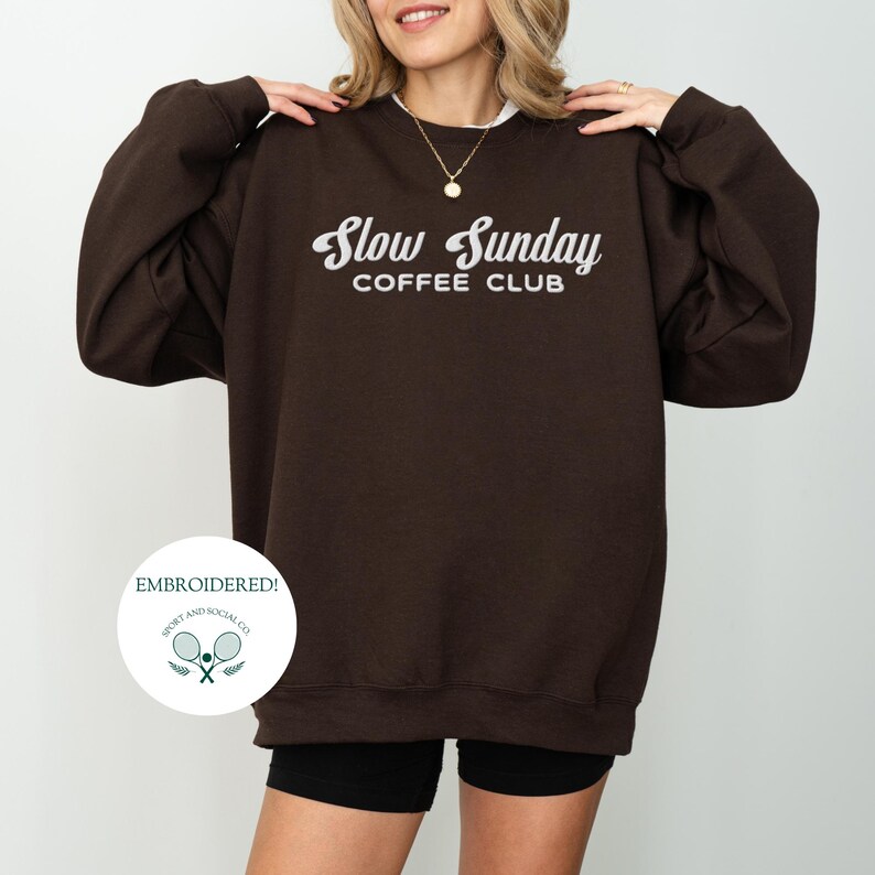 May include: Brown sweatshirt with the text "Slow Sunday Coffee Club" in white lettering. The sweatshirt is embroidered with a small logo of two tennis rackets and the text "Sport and Social Co."