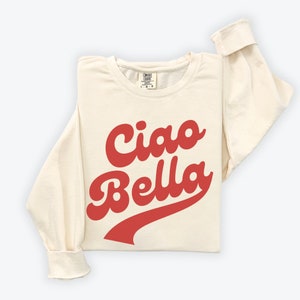 Puede incluir: Una sudadera de color crema con mangas largas y un gr&aacute;fico rojo de estilo retro que dice "Ciao Bella".