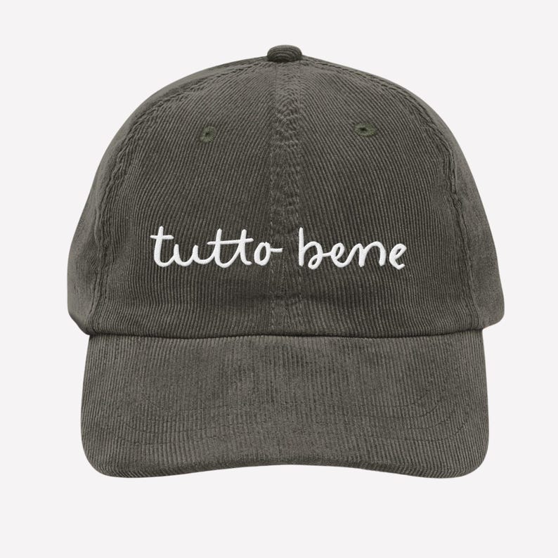 May include: A dark olive green corduroy baseball cap with the white cursive text "tutto bene" embroidered on the front. The cap has a curved brim and a fabric-covered button on top.