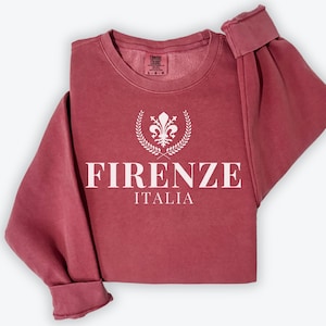 May include: A maroon sweatshirt with a white graphic design featuring a stylized fleur-de-lis with a wreath and the text "FIRENZE ITALIA".