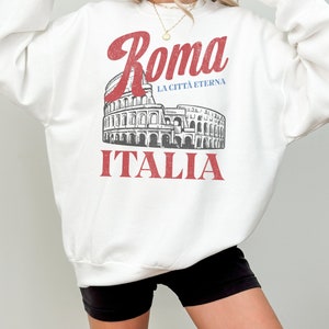 May include: White sweatshirt with a red graphic print of the Colosseum in Rome, Italy. The text "Roma" is in red, "La Citta Eterna" is in blue, and "ITALIA" is in red.
