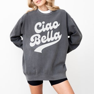Puede incluir: Una sudadera gris antracita con un estampado gr&aacute;fico blanco que dice "Ciao Bella" en una fuente retro.