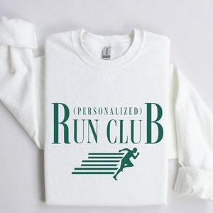 May include: White crewneck sweatshirt with the text "RUN CLUB" in dark green, with "(PERSONALIZED)" above. A graphic of a runner is below the text. The sleeves are rolled up.