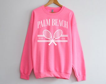 May include: Pink sweatshirt with white text that reads "Palm Beach Tennis Club" and a graphic of two crossed tennis rackets.