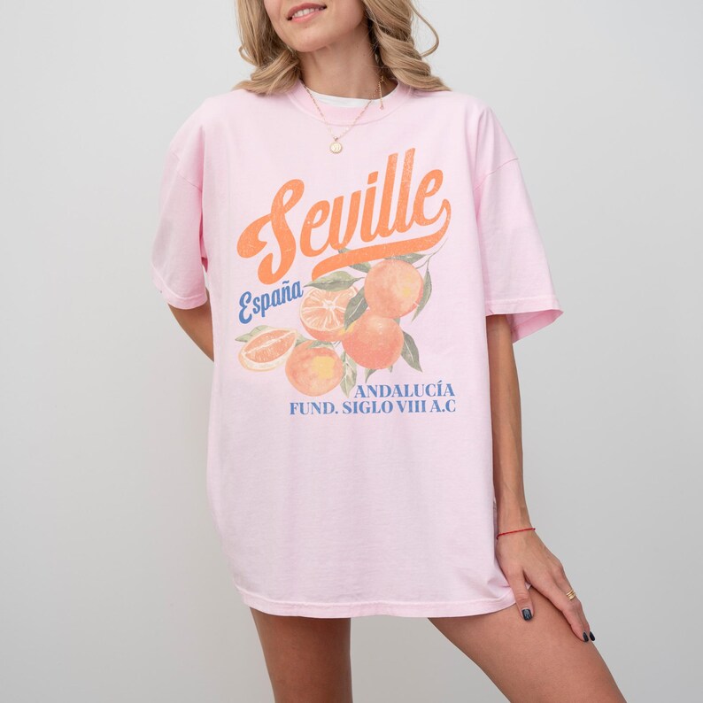 Pu&ograve; includere: Maglietta rosa oversize con una stampa grafica di arance e il testo "Sevilla, Espa&ntilde;a, Andaluc&iacute;a, Fund. Siglo VIII A.C."